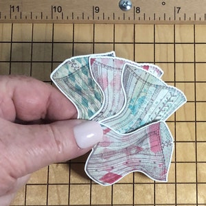 May include: Four vintage-style corsets in a stack, with a pink, blue, and green color scheme. The corsets are printed with a delicate floral pattern and have a lace trim.