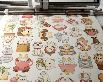 May include: A sheet of white paper with various stickers featuring cute cartoon cats in different poses and settings. The cats are depicted in various activities, such as drinking coffee, reading books, taking a bath, and relaxing on a pillow. The stickers are printed in bright colours and feature a variety of details, such as hearts, stars, and bubbles.