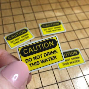 May include: Four yellow and black caution signs with the text "CAUTION DO NOT DRINK THIS WATER" on a wooden surface.