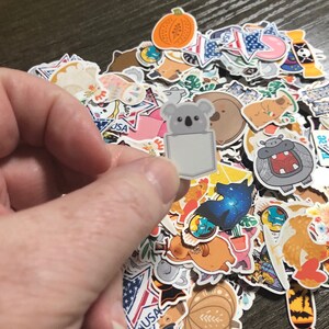 May include: A large collection of colorful stickers featuring various designs, including animals, food, and abstract patterns. One sticker features a koala with a pocket on its belly.