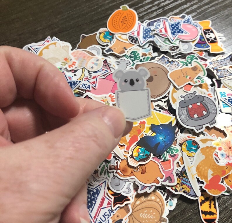 May include: A large collection of colorful stickers featuring various designs, including animals, food, and abstract patterns. One sticker features a koala with a pocket on its belly.