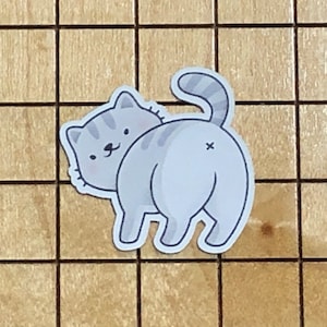 May include: A gray and white cartoon cat sticker with a striped tail. The cat is looking over its shoulder with a cute expression.