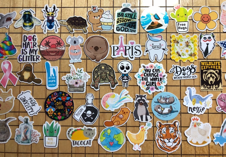 May include: A collection of colorful stickers featuring various designs, including animals, plants, and text. Some of the stickers have a humorous or inspirational message. The stickers are arranged on a wooden surface.