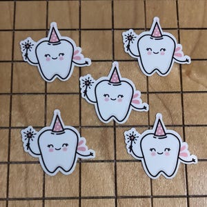 May include: Five white tooth-shaped stickers with black outlines. Each tooth has a pink party hat with white polka dots, pink fairy wings, and a smiling face. They are holding a magic wand with a star design.