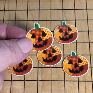 May include: A collection of pumpkin-shaped stickers with a patchwork design. Each sticker features a smiling jack-o'-lantern face with a green stem. The pumpkins have orange, yellow, and brown patterns, perfect for Halloween crafts and decorations.
