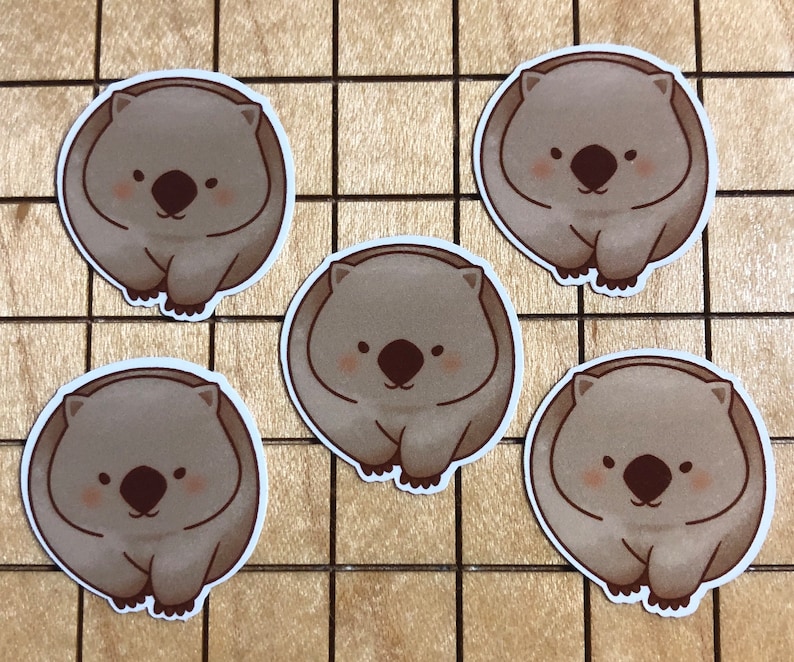Puede incluir: Cinco pegatinas de wombat de dibujos animados marrones y blancas sobre una superficie de madera marr&oacute;n claro. Cada pegatina presenta un wombat con una cara sonriente y orejas peque&ntilde;as y redondas.