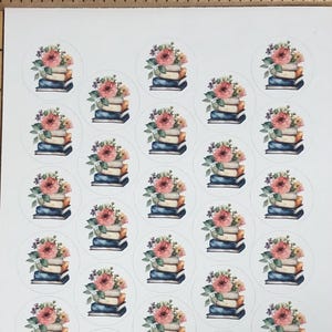 May include: A sheet of round stickers featuring watercolor illustrations. Each sticker shows a stack of books topped with a bouquet of pink and yellow flowers. The stickers are arranged in a grid pattern.