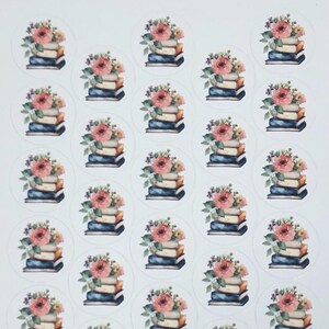 May include: Sheet of round stickers featuring stacks of books topped with floral arrangements. The books have blue, tan, and brown spines. The flowers are pink, peach, and purple. The stickers are on a white background.