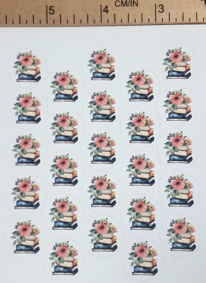 May include: Sheet of round stickers featuring stacks of books topped with floral arrangements. The books have blue, tan, and brown spines. The flowers are pink, peach, and purple. The stickers are on a white background.