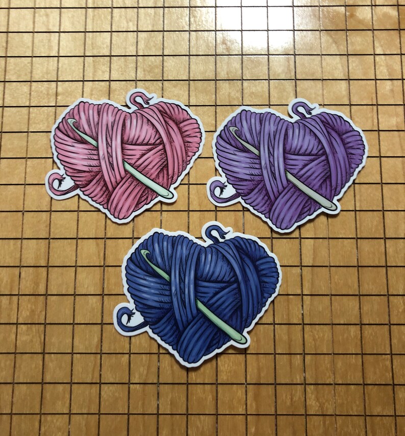 May include: Three heart-shaped yarn balls with a crochet hook through each. The yarn balls are pink, purple, and blue.
