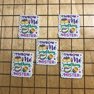 May include: Five white square stickers with a purple, green, and yellow Mardi Gras theme. The stickers say "Throw Me Something Mister".
