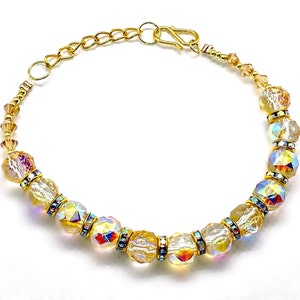 Op de afbeelding: Een gouden kettingarmband met regenboogkleurige kristallen kralen. De kralen zijn facetgeslepen en hebben een regenboogeffect.