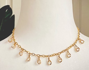 May include: A gold chain necklace with a delicate design featuring small, clear teardrop-shaped crystals dangling from the chain.