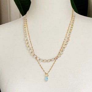 Op de afbeelding: Een delicate gouden ketting met een traanvormige hanger. De ketting is versierd met kleine, heldere, iriserende kralen.