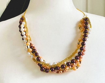 May include: A multi-strand necklace with brown, peach, and white pearls and gold accents.