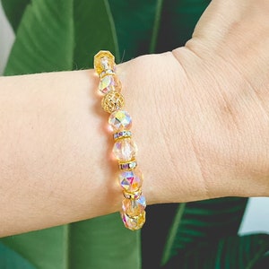 Op de afbeelding: Een gouden en regenboogkleurige kristallen kralen armband met een gouden accentbedel.