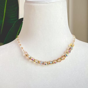 Op de afbeelding: Een delicate gouden ketting met iriserende glazen kralen. De ketting wordt getoond op een witte mannequinbuste.