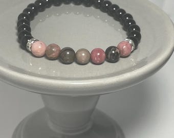 May include: A black and pink beaded bracelet with silver accents. The bracelet is made with black onyx and pink rhodochrosite beads.