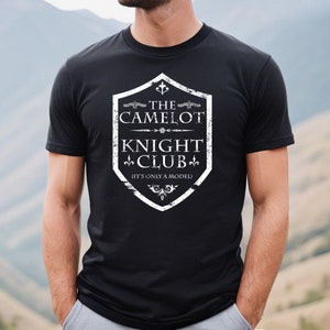 May include: Black t-shirt with a white graphic of a shield with the text "The Camelot Knight Club (It's only a model)"