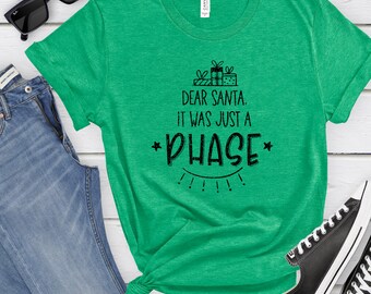 May include: Green t-shirt with a black graphic that says "Dear Santa. It was just a *PHASE*" with a star on either side of the word "PHASE" and a drawing of presents above the text.