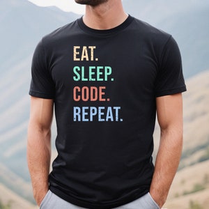 May include: Black t-shirt with the text "EAT. SLEEP. CODE. REPEAT." in colorful, distressed lettering.