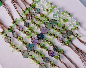 May include: A set of eight bracelets with green leaves and various colored crystal beads. The bracelets are made with brown cord and have small bells.