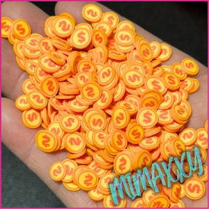 May include: A pile of orange and yellow plastic coin-shaped sprinkles with a dollar sign on each. The sprinkles are scattered on a hand.