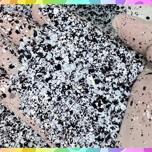 May include: Black and white glitter with a fine, speckled texture. The glitter is scattered on a surface and appears to be a craft supply.