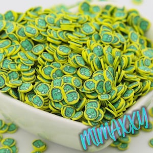 May include: A white bowl filled with yellow and green polymer clay slices. Each slice has a yellow border and a green cartoon face design. The slices are scattered, creating a textured, colorful appearance. The text "MIMAXXY" is in the bottom right corner.