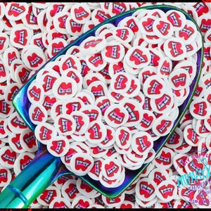 May include: A scoop filled with white and red round sprinkles with a vampire teeth design. The sprinkles are in a blue and purple scoop with a wooden handle.