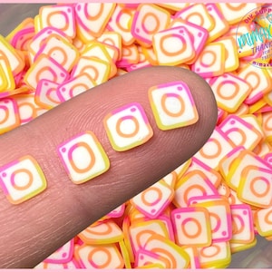 May include: A large quantity of small, colorful, square-shaped Instagram logo charms. The charms are pink, yellow, and white with a white outline. The charms are perfect for adding a touch of social media flair to crafts.