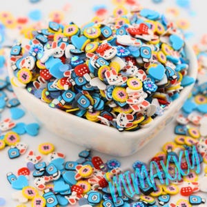 May include: A white bowl filled with colorful resin charms. The charms are shaped like hearts, flowers, bottles, and bunnies. The charms are perfect for adding a touch of whimsy to crafts and projects.