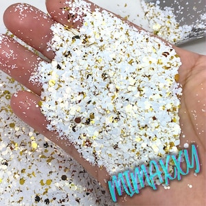 May include: White and gold glitter mix with different sizes and shapes of glitter. The glitter is in a hand, ready to be used for crafting projects.
