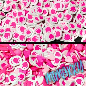 May include: A large pile of pink and white plastic charms in the shape of a woman's head with long hair. The charms are scattered on a white surface. The charms are small and perfect for adding a touch of whimsy to any project.