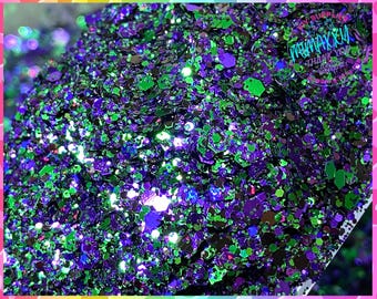 Op de afbeelding: Een close-up van groene en paarse glitter. De glitter is iriserend en heeft verschillende maten en vormen.
