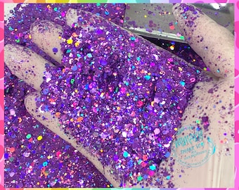 May include: Purple glitter with iridescent and rainbow accents. The glitter is in a hand, and the background is a white surface with a logo that says "Whimsy" and "Thank You for your patronage".