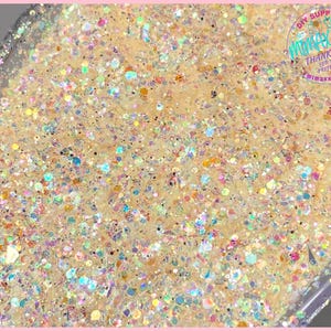 May include: A close-up of iridescent glitter in a variety of sizes and colors, including gold, silver, and white. The glitter is arranged in a random pattern and appears to be in a clear container.