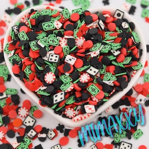 May include: A white heart-shaped bowl filled with colorful casino-themed sprinkles. The sprinkles are in the shape of playing cards, dice, poker chips, and dollar bills. The sprinkles are red, green, black, and white.