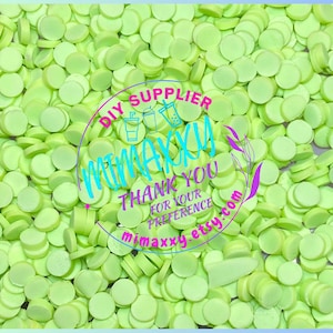 May include: A close-up image of a large quantity of small, bright green, round, flat, plastic circles. The circles are scattered randomly and appear to be a type of craft supply.