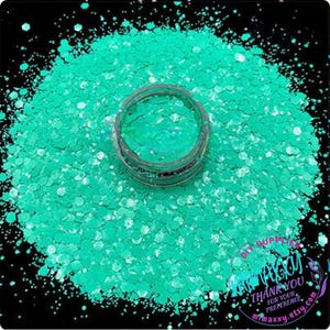 May include: A close-up of a jar of teal green glitter. The glitter is iridescent and has a holographic finish. The glitter is perfect for crafting, nail art, and resin projects.
