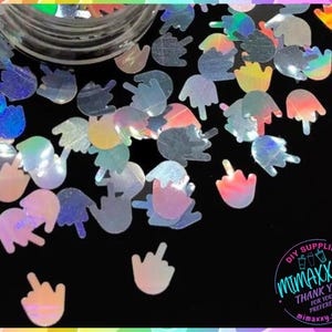 May include: A jar filled with iridescent holographic glitter shaped like middle fingers. The glitter is in various shades of blue, pink, and purple. The jar has a white label with the text "DIY SUPPLIER MIMAXXY THANK YOU FOR YOUR PREFERENCE MIMAXXY.ETSY.COM".