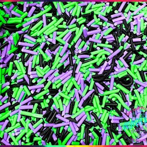 May include: A close-up image of a mixture of black, green, and purple sprinkles. The sprinkles are long and thin, and they are arranged in a random pattern.
