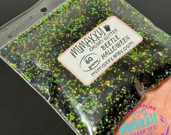 Op de afbeelding: Een zakje van 60 gram met zwarte en groene grove glitter met een holografische afwerking. Het zakje heeft een label met de tekst "Mimaxxxy Chunky Glitter Beetle Halloween mimaxxxy.etsy.com".