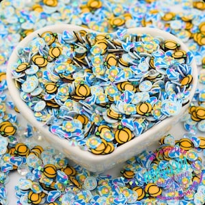 May include: A heart-shaped bowl filled with colorful polymer clay slices. The slices feature various designs, including pumpkins, teacups, and bunnies, in shades of yellow, blue, and white. These decorative pieces are ideal for crafting and embellishments.