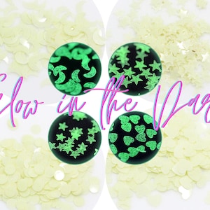 May include: Assortment of glow-in-the-dark sequins in various shapes, including stars, hearts, and moons. The sequins are shown in a close-up view, with some of them glowing brightly in the dark.
