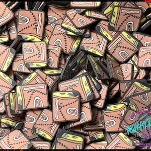 May include: A pile of small, brown, stitched book charms with yellow accents. The charms are made of resin and have a distressed, vintage look.