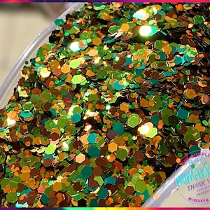 May include: A close-up of a container filled with green, gold, and brown glitter. The glitter is iridescent and has a variety of shapes and sizes.