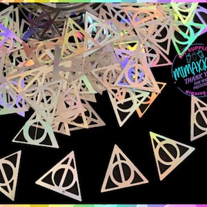 May include: A large quantity of iridescent holographic triangle-shaped confetti with a white outline of the Deathly Hallows symbol. The confetti is scattered on a black background.