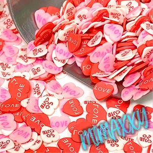 May include: A large pile of small pink and red heart-shaped sprinkles with white lettering. The lettering says "love", "cute", and "so cute".