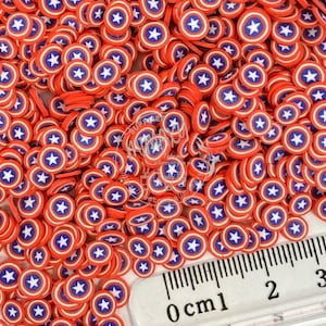 May include: A close-up of a pile of red, white, and blue star-shaped confetti. The confetti is about 1 cm in diameter and is arranged in a random pattern. A ruler is visible in the bottom right corner of the image.